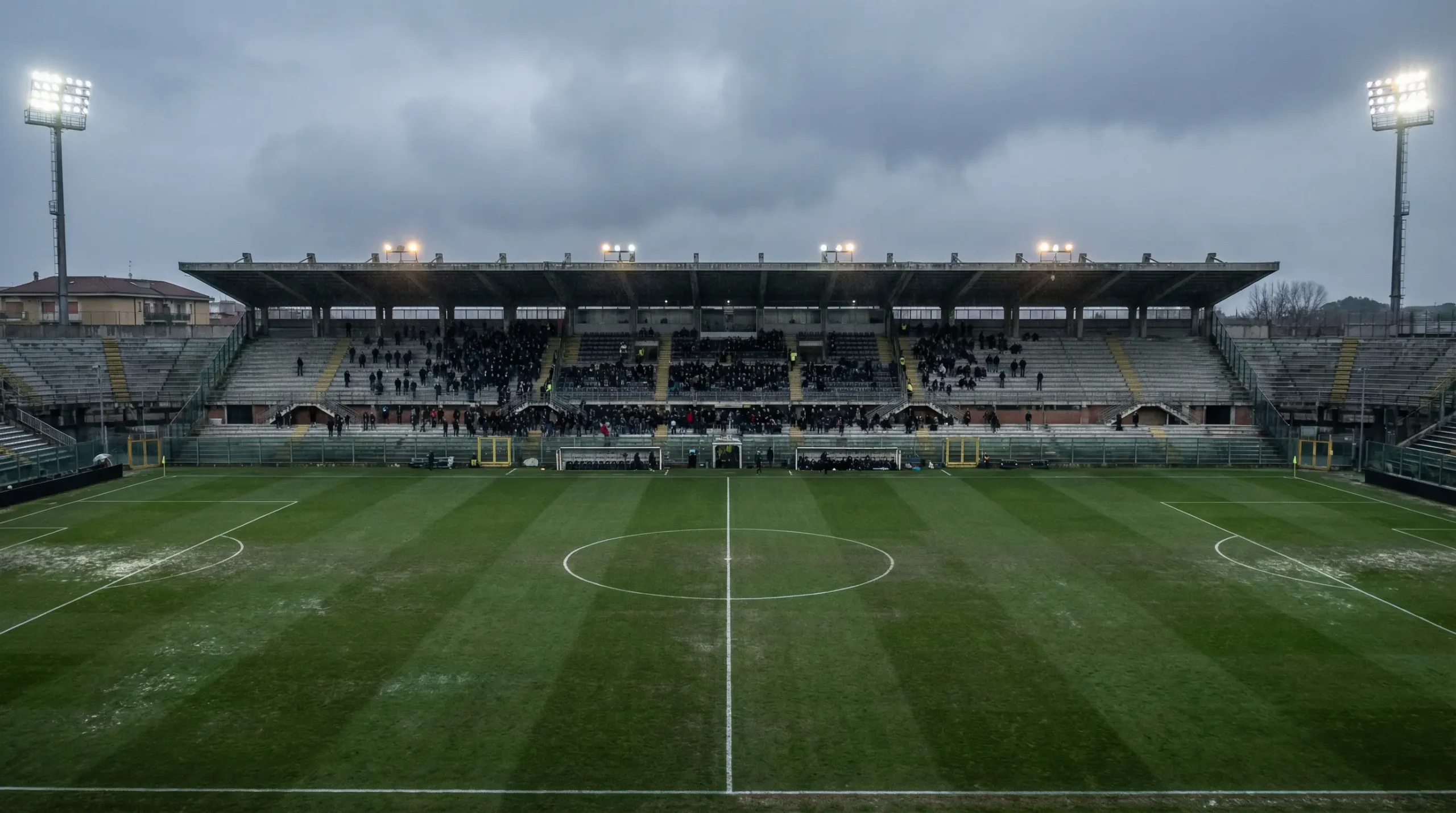 Stadio di calcio semivuoto con tribune in ombra, atmosfera malinconica di fine stagione